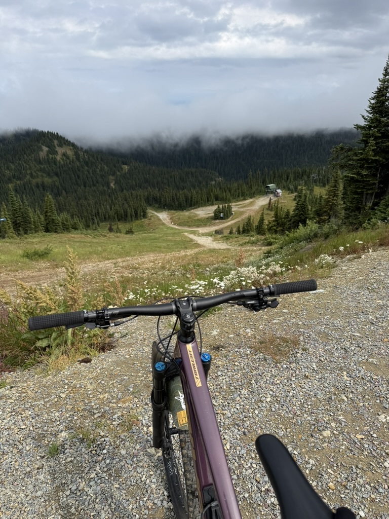Handlebars pointed down a gravel ski-run access road toward a fog-covered ridge of pines at Big Mountain in Whitefish, Montana