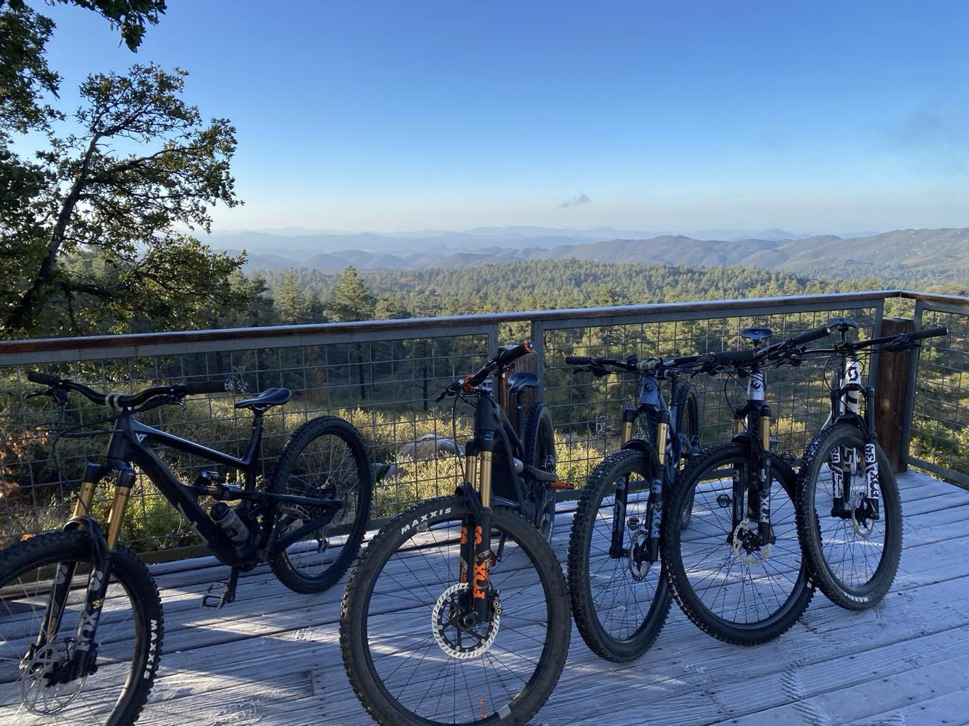 Five mountain bikes lined up on a wooden overlook deck above forested hills