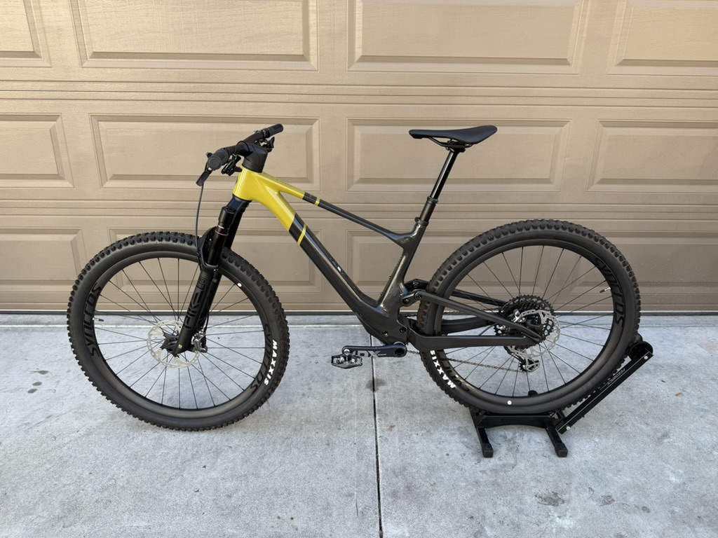 A clean full-suspension mountain bike on a stand in front of a garage door, lit evenly from the side - the listing photo a buyer wants to see