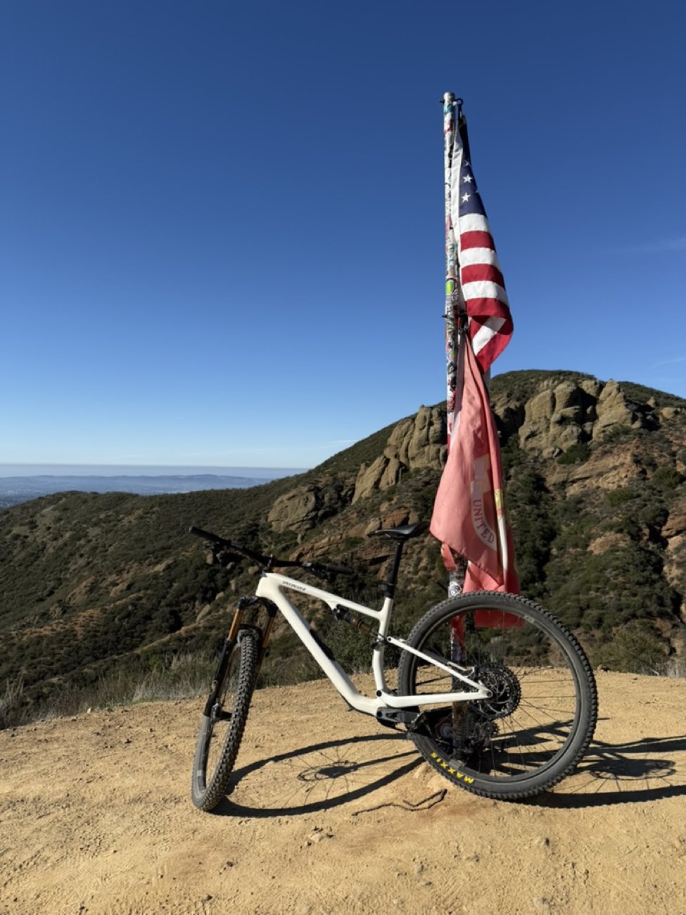Mountain bike parked at a summit next to a flag pole above the hills
